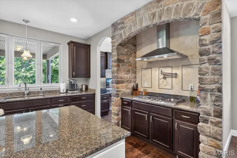 Stone archway surrounding the stainless steel range hood, built-in gas cooktop, and pot filler — 1307 Homestead Heights Drive, Wildwood, MO 63005