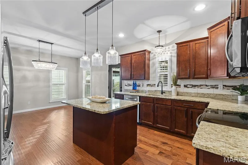 Kitchen featuring wood-finish flooring, an island with a light-toned countertop, dark wood cabinetry, and a tile backsplash — 3222 Starkville Street, St Charles, MO 63301