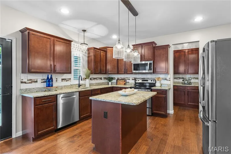 Kitchen featuring wood-finish flooring, dark wood cabinetry, granite countertops, and stainless steel appliances — 3222 Starkville Street, St Charles, MO 63301