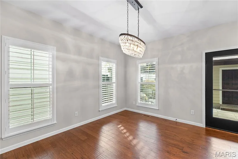 Hardwood-finish flooring, three windows with plantation shutters, a contemporary chandelier, and a black-framed glass-paneled door — 3222 Starkville Street, St Charles, MO 63301