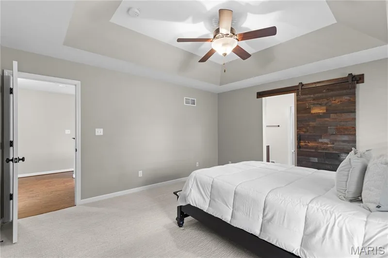 Tray ceiling, ceiling fan with light fixture, light-toned carpeting, wood-paneled barn door, and neutral wall tones — 3222 Starkville Street, St Charles, MO 63301