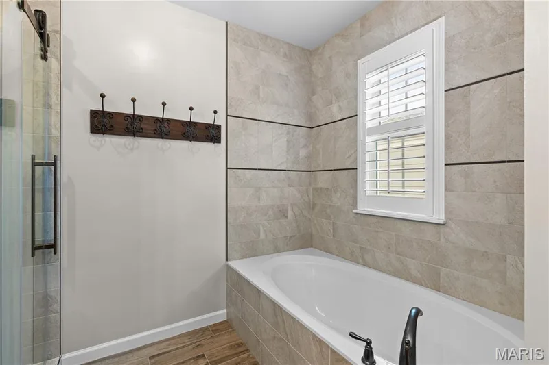 Built-in soaking tub with dark bronze fixtures, tile surround, and wood-finish flooring — 3222 Starkville Street, St Charles, MO 63301