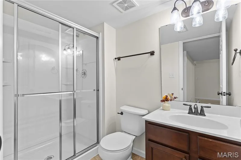 Shower enclosure with glass sliding doors, dark wood-finish vanity, white countertop, white undermount sink, and bronze-finish fixtures — 3222 Starkville Street, St Charles, MO 63301