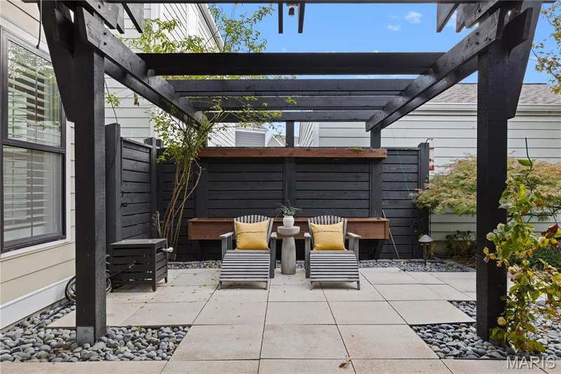 Patio featuring a dark wood pergola, stone paver flooring, black privacy fencing, and river rock landscaping — 3222 Starkville Street, St Charles, MO 63301