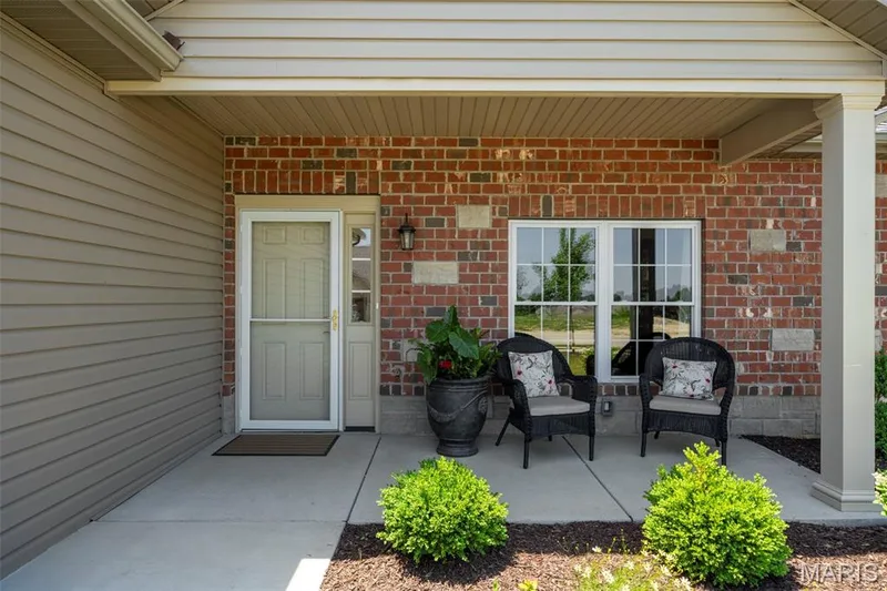 Covered concrete porch featuring brick and siding exterior, a white entry door with a screen door, and a white-framed window — 193 Santa Elena Drive, Wentzville, MO 63385