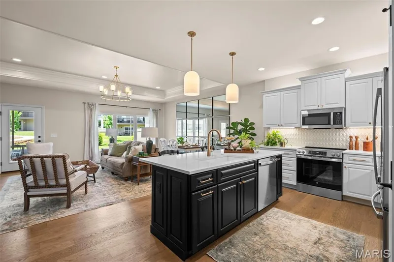 Kitchen island with a white countertop and gold-toned faucet, stainless steel appliances, light gray upper cabinetry, wood-finish flooring, and a tray ceiling with recessed lighting — 193 Santa Elena Drive, Wentzville, MO 63385