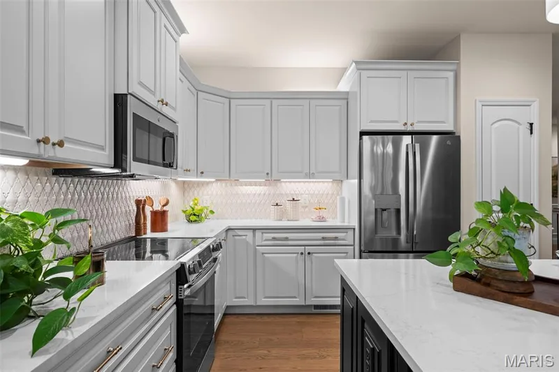 Light gray cabinetry with crown molding, stainless steel appliances, solid surface countertops, patterned tile backsplash, and wood-finish flooring — 193 Santa Elena Drive, Wentzville, MO 63385