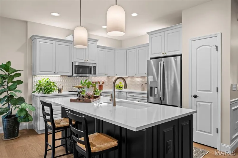 Kitchen featuring a central island with a solid surface countertop, stainless steel appliances, light-toned cabinetry, wood-finish flooring, and pendant lighting — 193 Santa Elena Drive, Wentzville, MO 63385