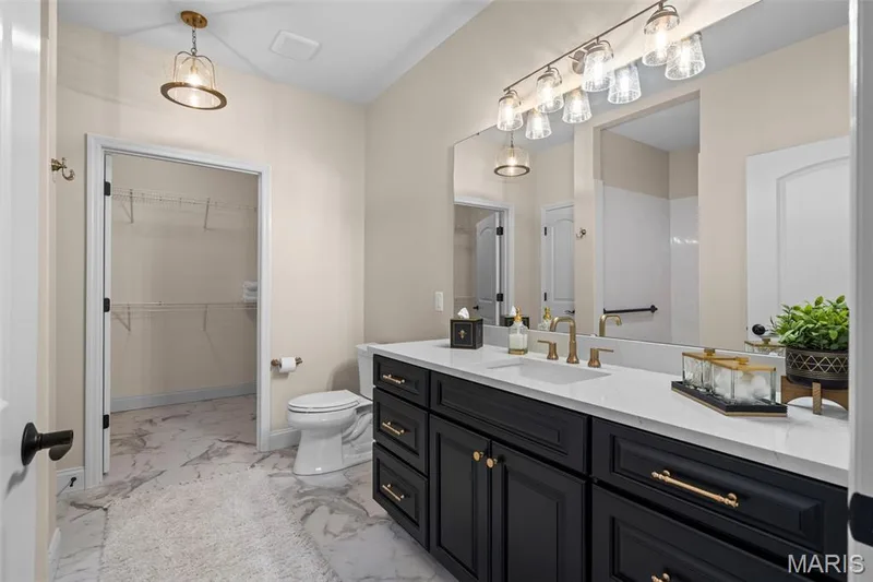 White marble-look flooring, dual-sink vanity with dark cabinetry, integrated vanity lighting, large wall mirror, and walk-in closet with wire shelving — 193 Santa Elena Drive, Wentzville, MO 63385
