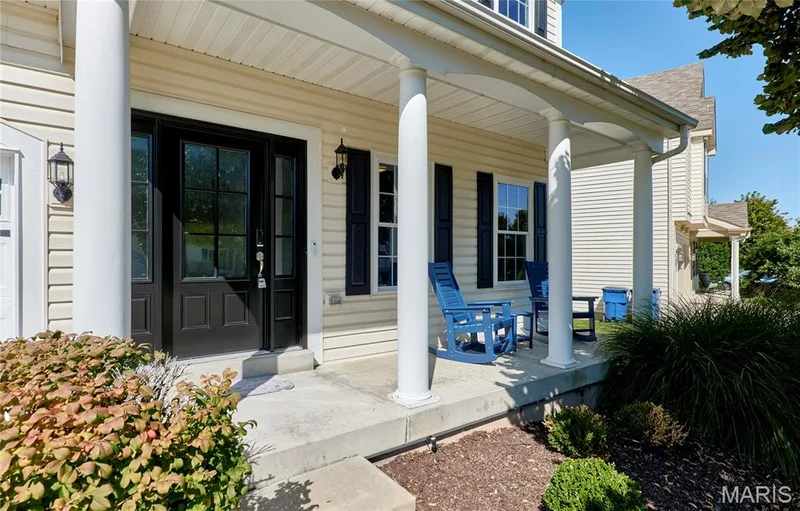 Welcoming front porch featuring white columns, a covered pergola, black multi-panel entry door, horizontal siding exterior, landscape lighting, and manicured planting beds with ornamental grasses and seasonal plantings — 264 Greenshire Lane, Dardenne Prairie, MO 63368