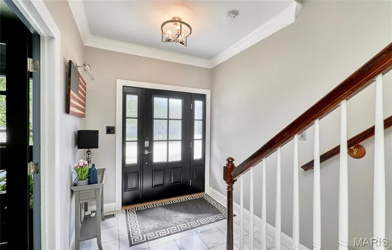 Welcoming foyer featuring black six-panel entry doors with sidelights, geometric patterned tile flooring, white wainscoting, dark wood stair railing, and recessed ceiling detail with pendant lighting fixture — 264 Greenshire Lane, Dardenne Prairie, MO 63368