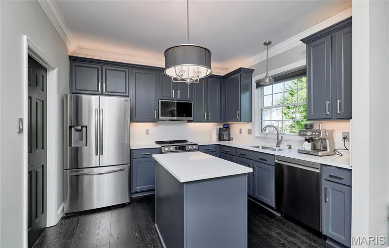 Modern kitchen featuring dark cabinetry with chrome hardware, white quartz countertops, a center island with seating space, stainless steel appliances including a French-door refrigerator and gas cooktop, dark wood-finish flooring, and a pendant light fixture overhead — 264 Greenshire Lane, Dardenne Prairie, MO 63368