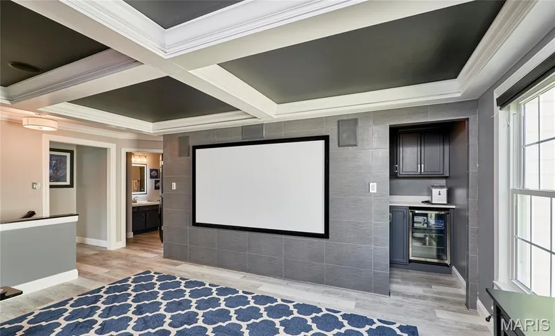 Coffered ceiling with dark gray panels, built-in entertainment screen, integrated wet bar with lower beverage refrigerator, wood-finish flooring, and white trim window — 264 Greenshire Lane, Dardenne Prairie, MO 63368