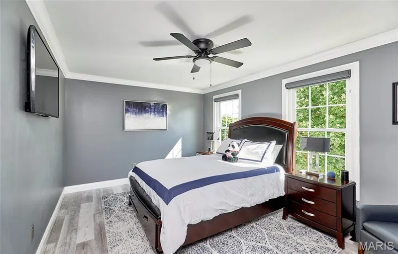 Bright secondary bedroom featuring soft gray walls, ceiling fan with integrated lighting, wood-finish flooring, and large multi-pane windows providing natural light — 264 Greenshire Lane, Dardenne Prairie, MO 63368