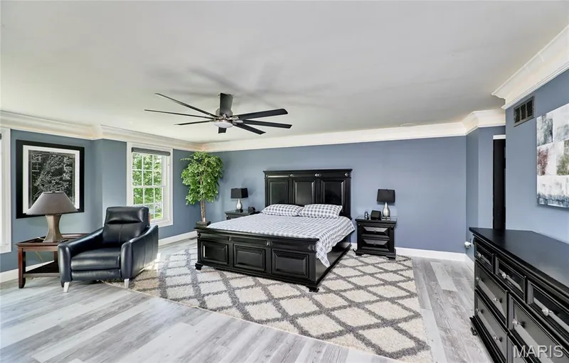 Spacious primary bedroom showcasing soft blue walls, gleaming wood-finish flooring, and a geometric area rug — 264 Greenshire Lane, Dardenne Prairie, MO 63368