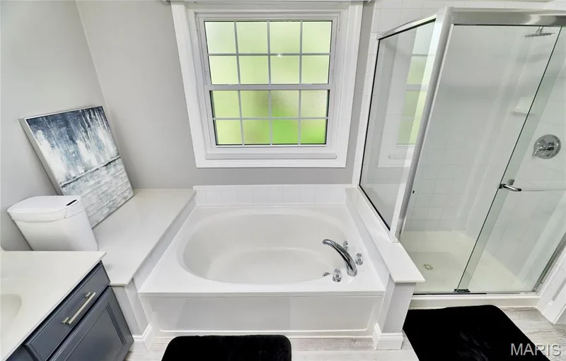Spa-inspired master bath featuring a deep soaking tub with dual fixtures, frameless glass shower enclosure, white subway tile surround, and abundant natural light from a large skylight window — 264 Greenshire Lane, Dardenne Prairie, MO 63368