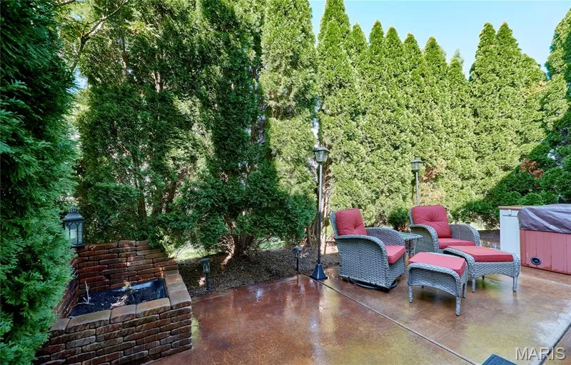 Stained concrete patio with a built-in brick fire pit, surrounded by mature evergreen trees, and equipped with a covered hot tub — 264 Greenshire Lane, Dardenne Prairie, MO 63368
