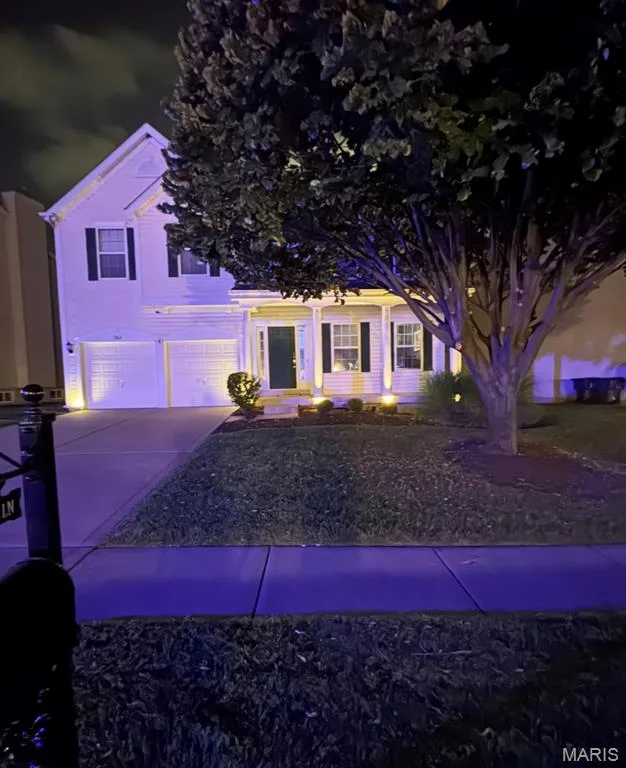 Two-story colonial home illuminated by professional landscape lighting, featuring a two-car garage, manicured front lawn, and mature shade trees — 264 Greenshire Lane, Dardenne Prairie, MO 63368