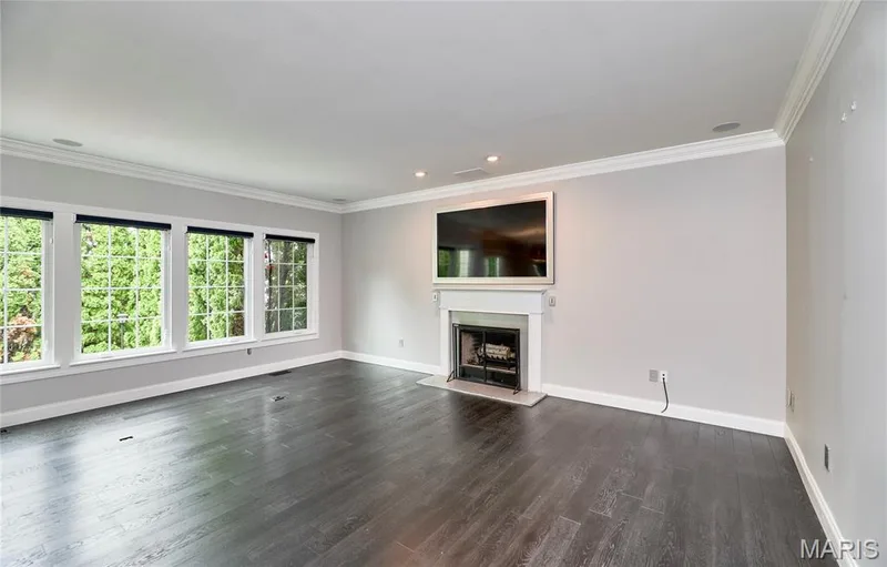 Dark wood-finish flooring, multiple pane windows, crown molding, a white mantel, and a fireplace with a dark surround — 264 Greenshire Lane, Dardenne Prairie, MO 63368