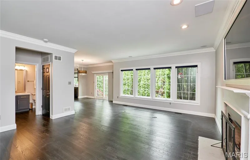 Expansive living area with dark wood-finish flooring, a white mantel, and crown molding — 264 Greenshire Lane, Dardenne Prairie, MO 63368