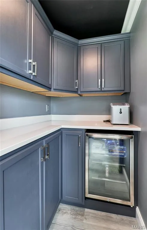 Blue shaker-style cabinetry with chrome hardware, white solid surface countertops, built-in beverage refrigerator, and wood-finish flooring — 264 Greenshire Lane, Dardenne Prairie, MO 63368