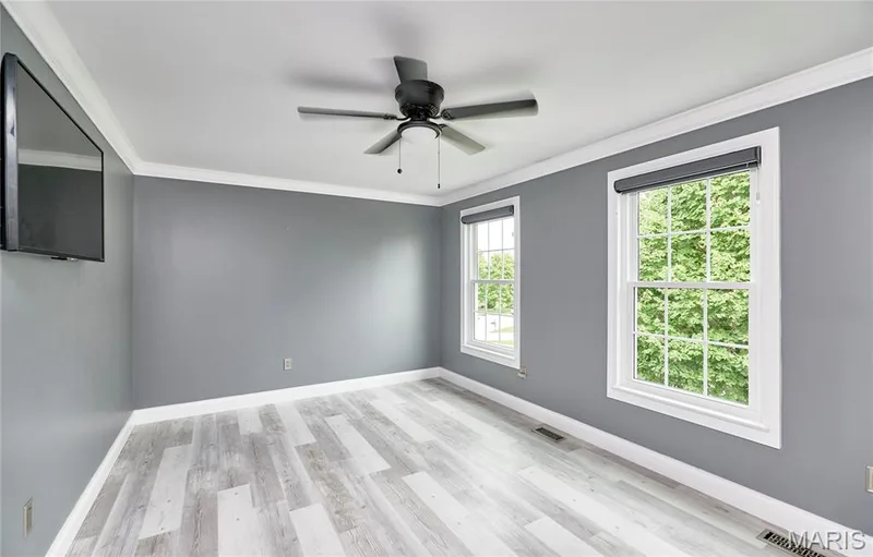 Light gray wood-finish flooring, white crown molding, gray painted walls, two double-hung windows, and a ceiling fan — 264 Greenshire Lane, Dardenne Prairie, MO 63368