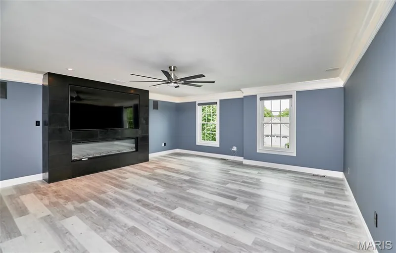 Expansive room featuring wood-finish flooring, a built-in media console with an integrated linear fireplace, and two large windows — 264 Greenshire Lane, Dardenne Prairie, MO 63368