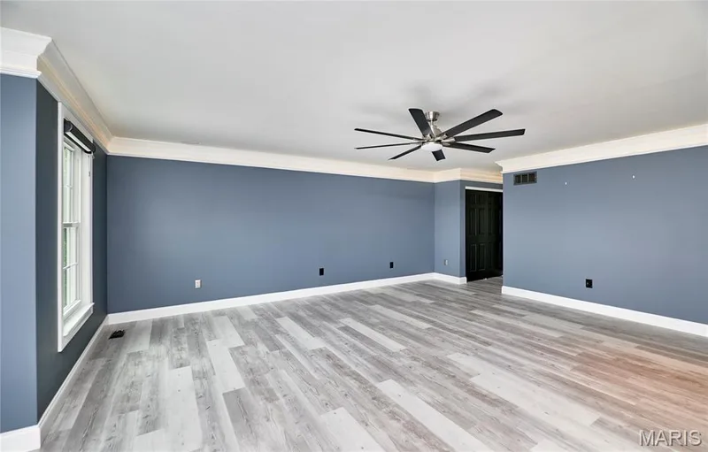 Spacious room featuring wood-finish flooring, crown molding, and a modern ceiling fan — 264 Greenshire Lane, Dardenne Prairie, MO 63368