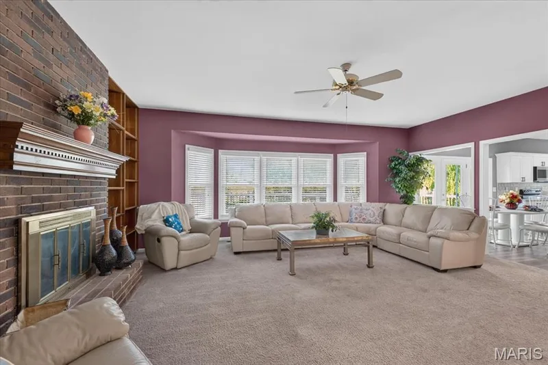 Brick woodburning fireplace with a decorative mantel and hearth, built-in shelving, ceiling fan, and carpeted flooring — 3445 Riverchase Parkway, St Charles, MO 63301