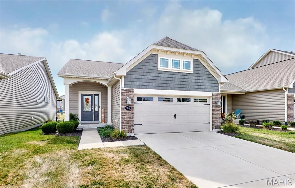 Exterior featuring a covered entryway, brick accents, shake siding, a two-car garage with windows, and a paved driveway — 305 Copperfield Court, St Charles, MO 63301