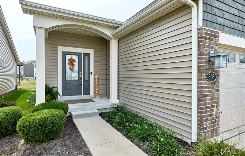Covered front entry with an arched portico, brick accent column, and a paneled garage door — 305 Copperfield Court, St Charles, MO 63301