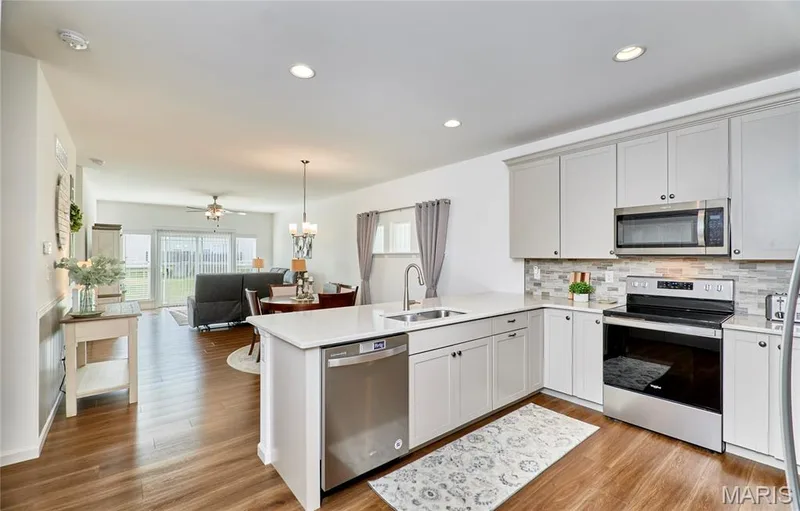 Open-concept kitchen with light-colored cabinetry, stainless steel appliances, and wood-finish flooring — 305 Copperfield Court, St Charles, MO 63301