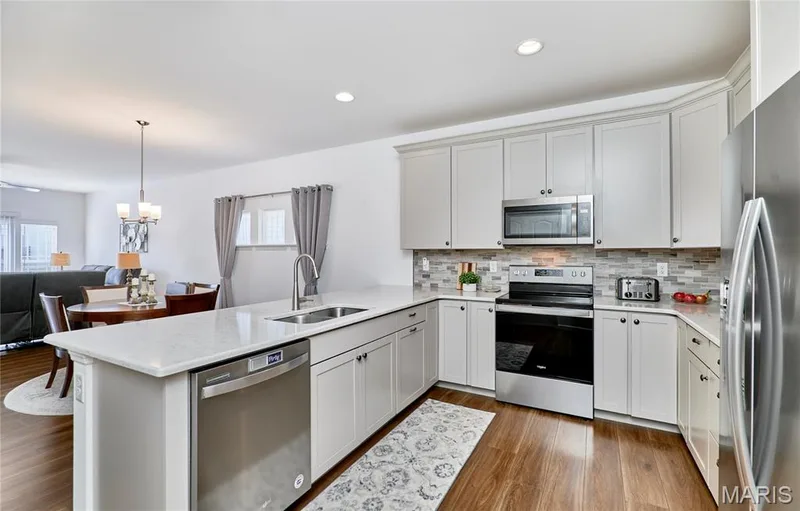 Kitchen with wood-finish flooring, white cabinetry, integrated stainless steel appliances, and a mosaic tile backsplash — 305 Copperfield Court, St Charles, MO 63301