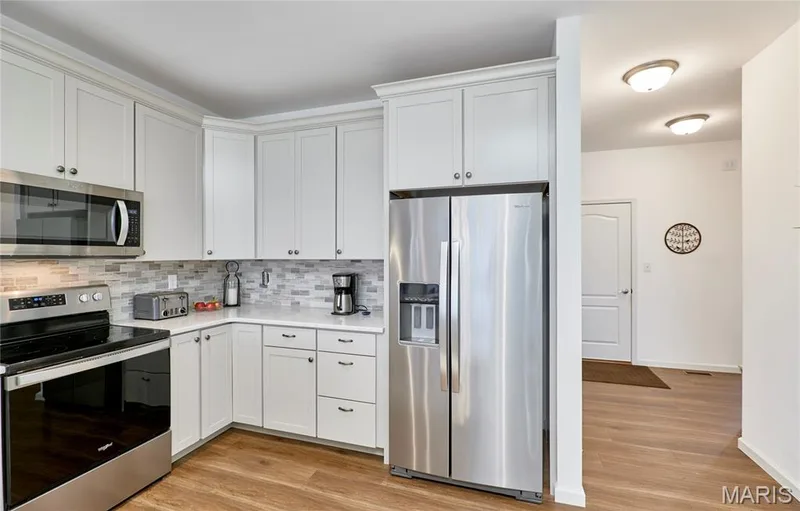 White shaker cabinetry with modern hardware, stainless steel appliances, mosaic tile backsplash, wood-finish flooring, and recessed ceiling lighting — 305 Copperfield Court, St Charles, MO 63301