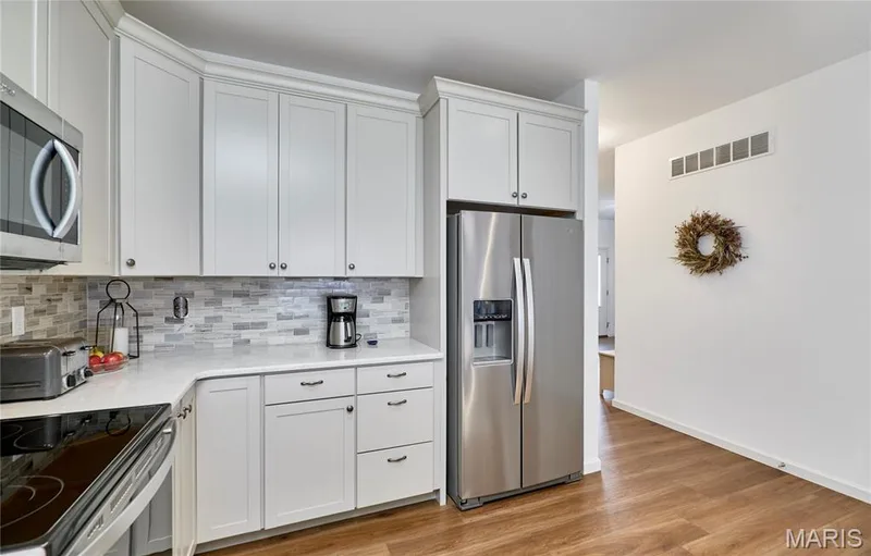 White cabinetry with crown molding, stainless steel appliances, a tile backsplash, and wood-finish flooring — 305 Copperfield Court, St Charles, MO 63301