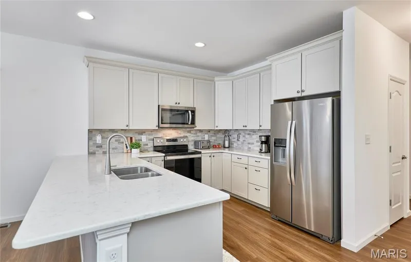 Kitchen featuring light-toned cabinetry, stainless steel appliances, a tile backsplash, wood-finish flooring, and recessed lighting — 305 Copperfield Court, St Charles, MO 63301