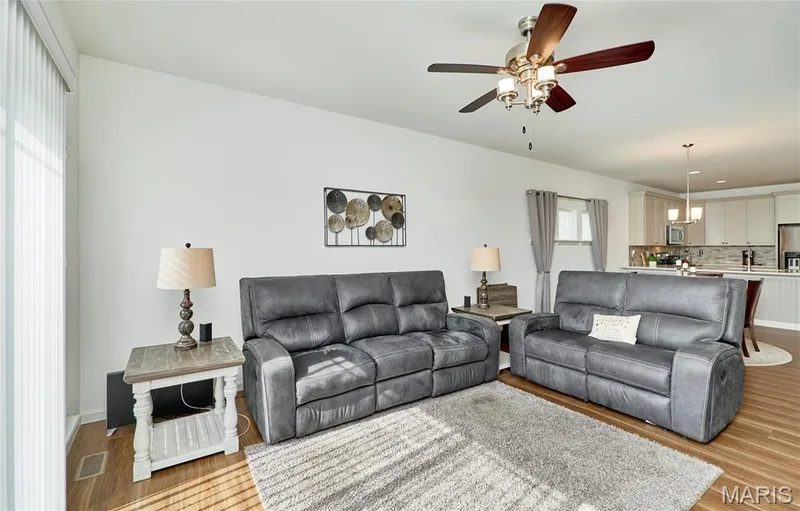 Open-concept living space featuring wood-finish flooring, a ceiling fan with integrated lighting, and white vertical blinds — 305 Copperfield Court, St Charles, MO 63301