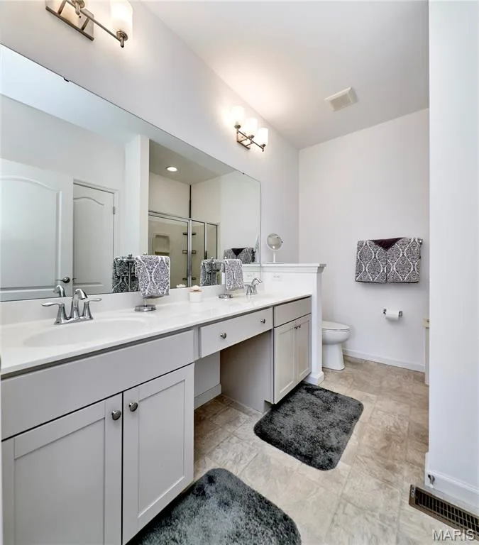 Dual vanities with undermount sinks, expansive countertop, built-in cabinetry, large wall-mounted mirror, and tile flooring — 305 Copperfield Court, St Charles, MO 63301
