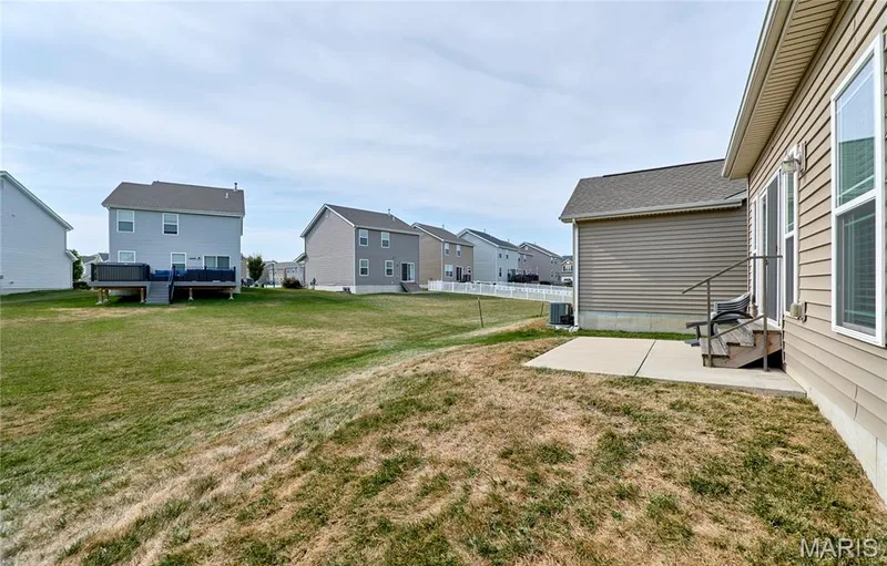 Expansive backyard with a concrete patio, exterior siding, and a wooden staircase with a metal railing — 305 Copperfield Court, St Charles, MO 63301