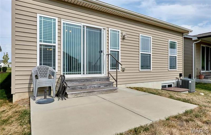 Back exterior featuring tan horizontal siding, multiple double-hung windows, and a sliding glass door — 305 Copperfield Court, St Charles, MO 63301