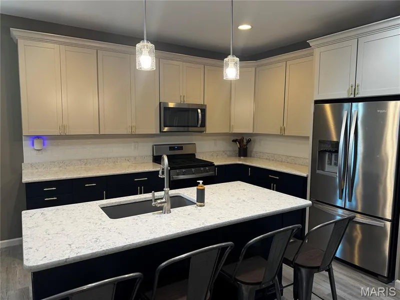 Kitchen with two-tone cabinetry, stainless steel appliances, a center island with sink, pendant lighting, and wood-finish flooring — 401 Copperfield Court, St Charles, MO 63301