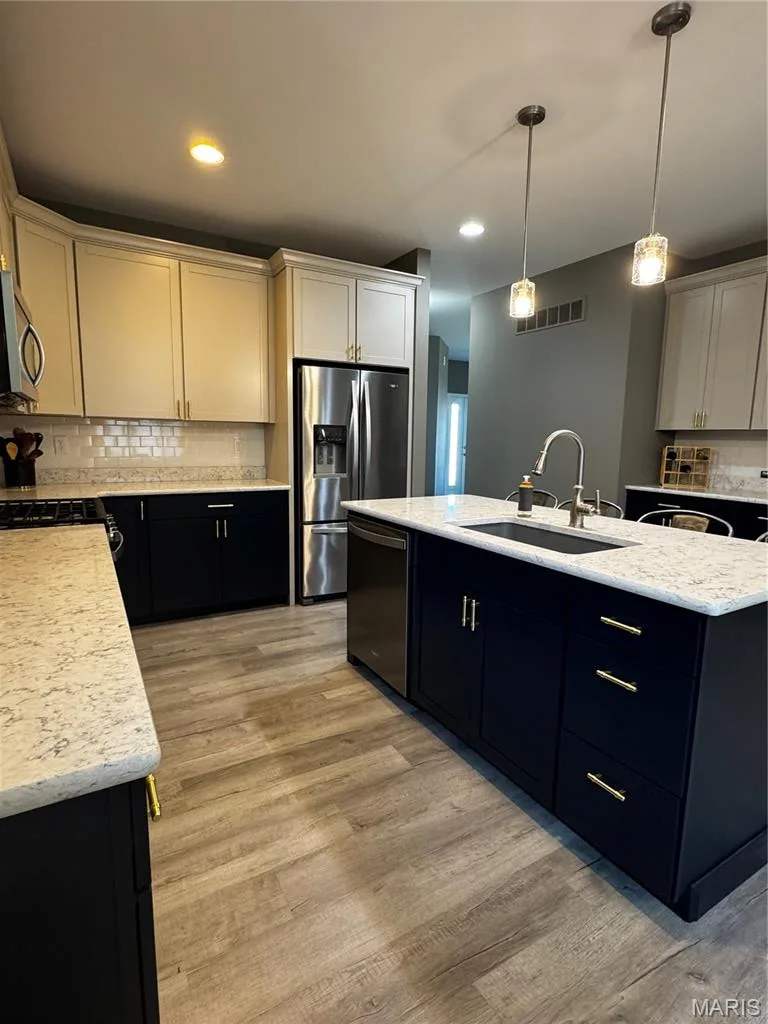 Two-tone cabinetry with gold-toned hardware, stainless steel appliances, wood-finish flooring, and a central island with a built-in sink — 401 Copperfield Court, St Charles, MO 63301