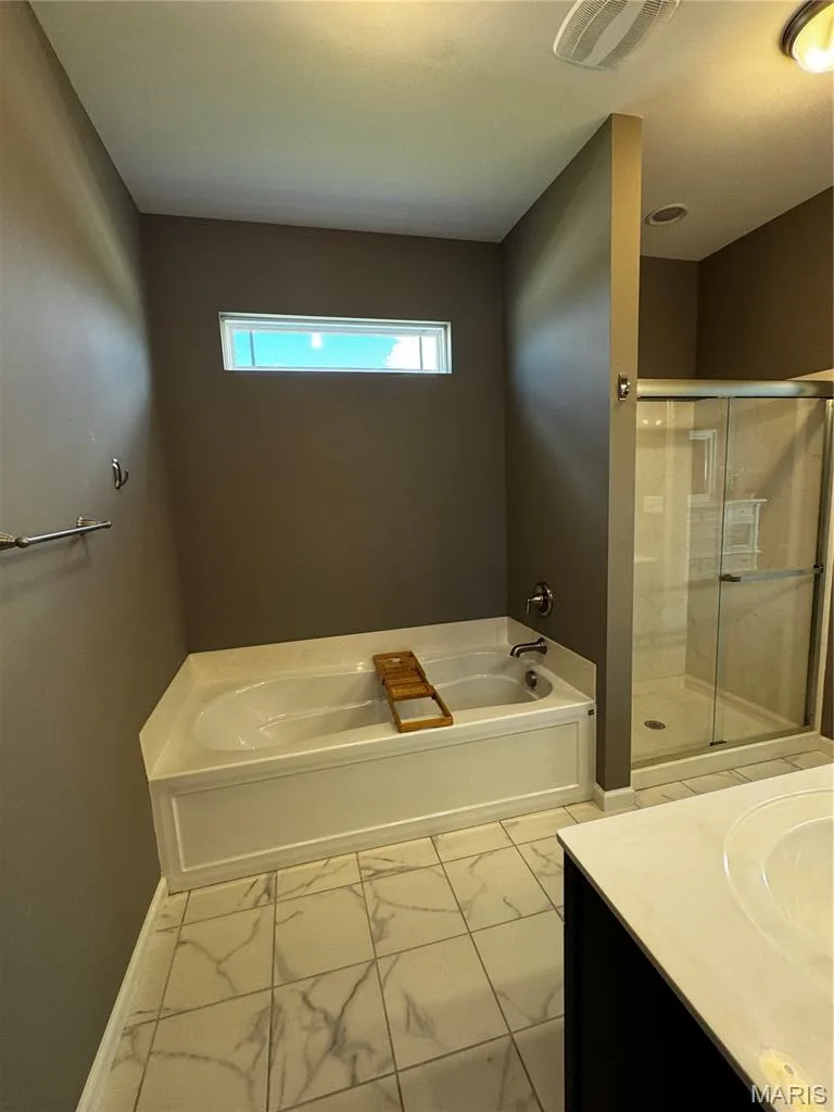 Built-in bathtub, glass-enclosed shower, single vanity with integrated sink, rectangular transom window, and patterned tile flooring — 401 Copperfield Court, St Charles, MO 63301