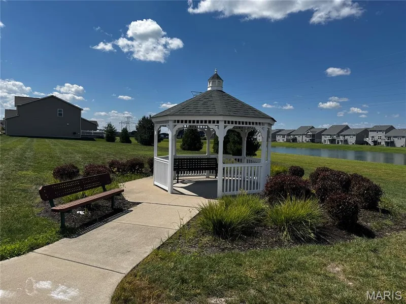 White gazebo with green roof, concrete pathway, and landscaping with shrubs, situated beside a pond — 401 Copperfield Court, St Charles, MO 63301