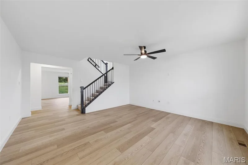 Open-concept living space featuring wood-finish flooring, a modern ceiling fan, and a staircase with black railings — 8 Shady Elm Court, St Charles, MO 63301