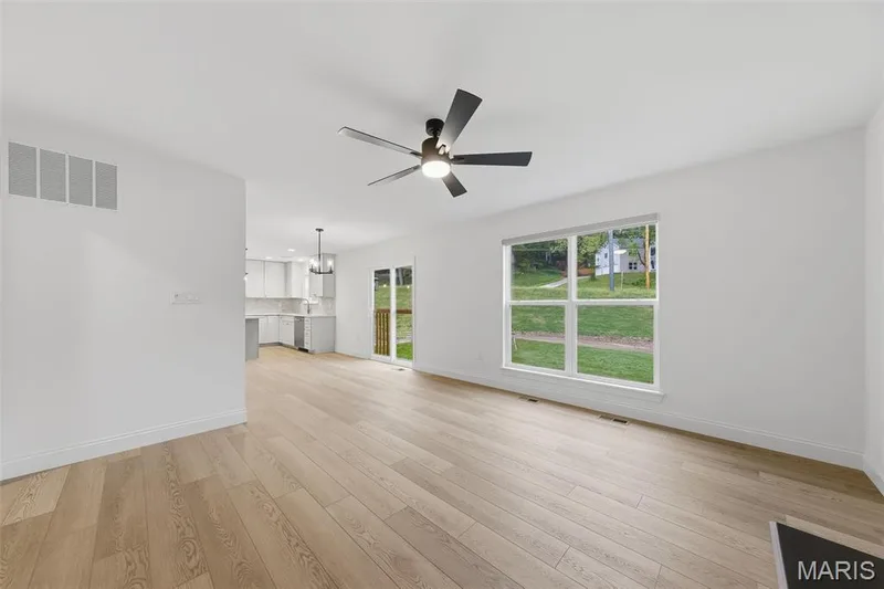 Light wood-finish flooring, a contemporary ceiling fan with integrated lighting, a large multi-pane window, and a sliding glass door providing exterior access — 8 Shady Elm Court, St Charles, MO 63301