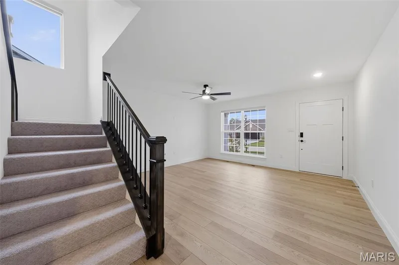 Light wood-finish flooring, white paneled entry door, black ceiling fan, and carpeted stairs with dark wood newel post and balusters — 8 Shady Elm Court, St Charles, MO 63301
