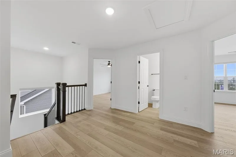 Wood-finish flooring, recessed lighting, white interior doors, dark wood stair banister with metal spindles, and an attic access panel — 8 Shady Elm Court, St Charles, MO 63301