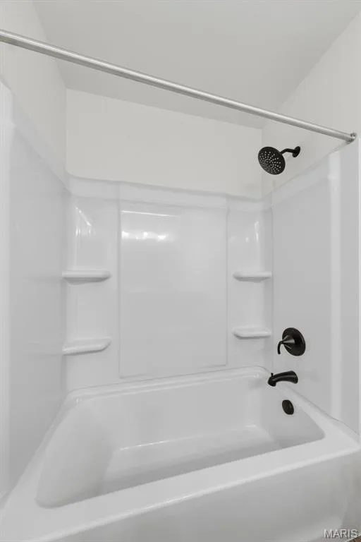 White bathtub with integrated shower, matte black fixtures, and built-in shelving — 8 Shady Elm Court, St Charles, MO 63301