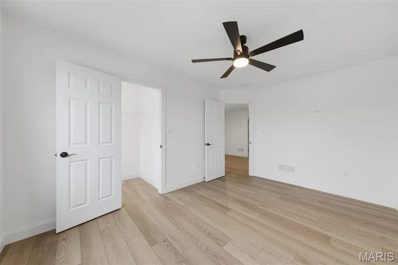 Expansive room featuring wood-finish flooring, a modern black ceiling fan with integrated lighting, white walls, and a closet with a built-in wire shelf — 8 Shady Elm Court, St Charles, MO 63301